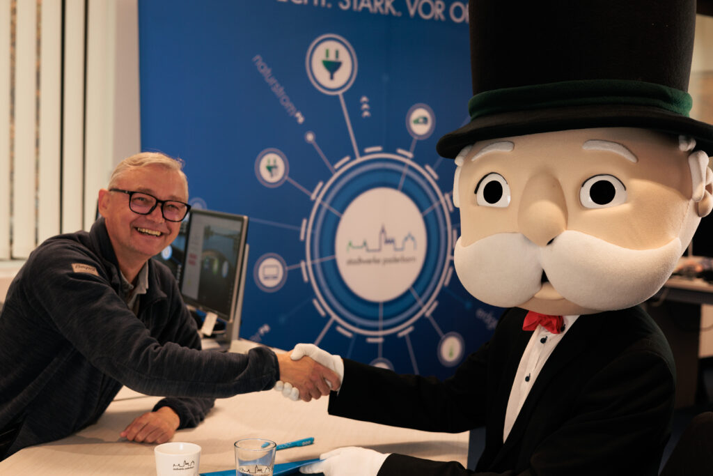 Geschäftsführer Christian Müller reicht Monopoly Maskottchen die Hand