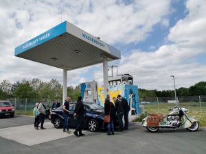 Personen, ein Auto und ein Motorrad an einer Wasserstoff-Tankstelle